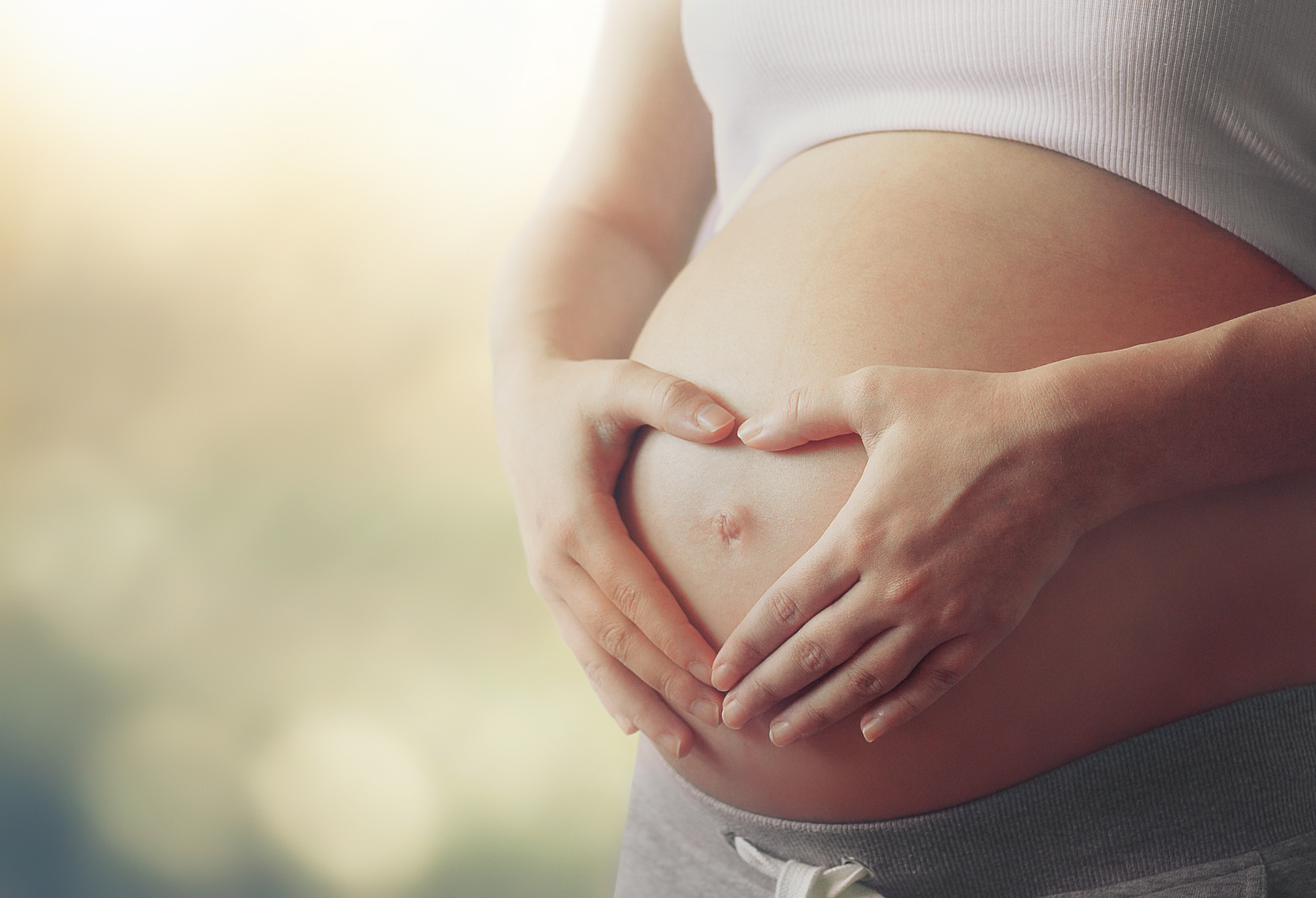 Mutter formt mit ihren Händen ein Herz auf ihrem Babybauch